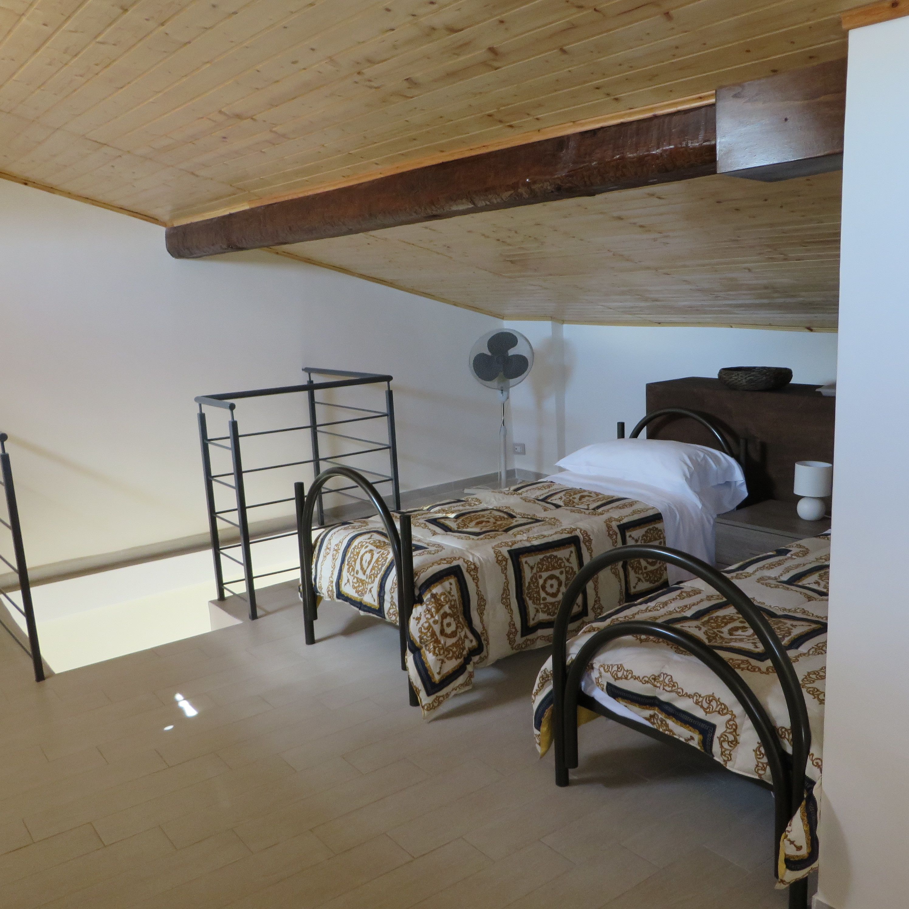 Un dormitorio con dos camas, un ventilador y techo de madera.