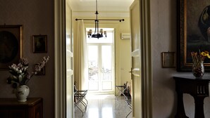 A hallway with a chandelier, a door leading to a balcony, and a vase with flowers on a table. - Al Teatro Massimo Home (Catania)