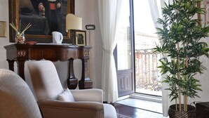 A room with a large window, a potted plant, a framed portrait, and a wooden desk with a lamp. - Al Teatro Massimo Home (Catania)