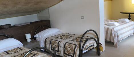 A dormitory room with three beds, wooden beams on the ceiling, and a small table with a lamp.