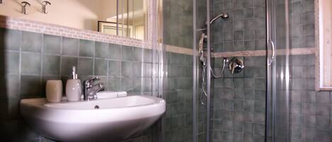 A bathroom with a glass-enclosed shower, a sink with a mirror, and green-tiled walls.