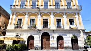 A multi-story building with a yellow facade, arched doorways, and balconies with plants. - Al Teatro Massimo Home (Catania)
