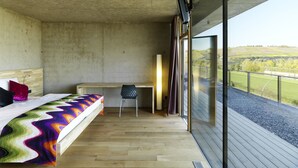Een slaapkamer met een bed, een bureau en een groot raam met uitzicht op het platteland.