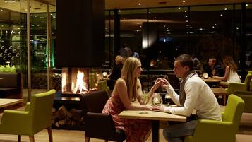 A cozy restaurant with a fireplace, wooden tables, and green chairs.