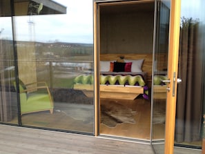 Une chambre à coucher avec un lit en bois, une chaise verte et une porte en verre donnant sur un balcon.