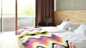 A modern hotel room with a large bed, a wooden headboard, a view of greenery outside, and a balcony.