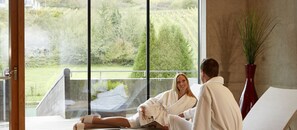 A couple sitting on a balcony with a view of a garden and a lake. - Hotel Ecluse (Stadtbredimus)