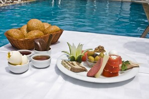 A table with a variety of food items including bread, cheese, and olives, set by a pool. - Zel Hotel (Konyaalti)