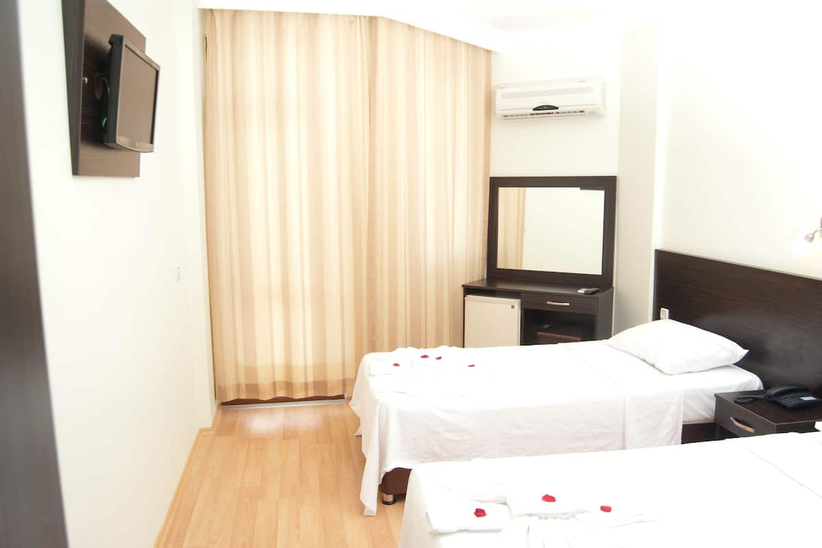 A hotel room with two beds, a desk, a mirror, an air conditioner, and a television.