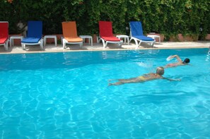 A swimming pool with clear blue water, surrounded by lounge chairs in various colors. - Zel Hotel (Konyaalti)