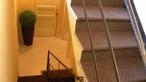 Una escalera con peldaños alfombrados y barandillas metálicas que conduce a una puerta, con una planta en maceta a su lado.