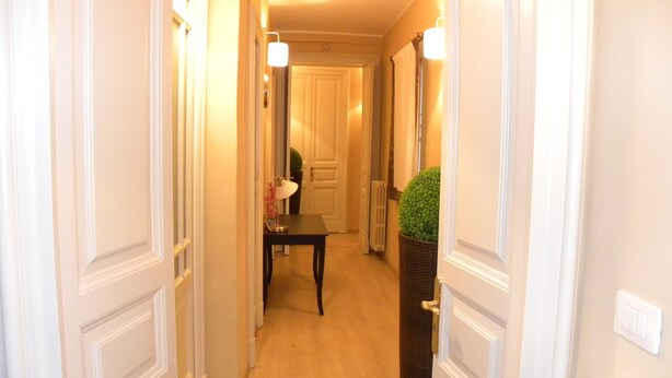 Un pasillo con suelo de madera, puertas blancas y una pequeña mesa con lámpara.
