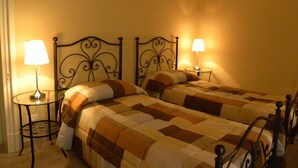 Una cama doble con una colcha a cuadros, dos lámparas de noche y un cuadro colgado en la pared.