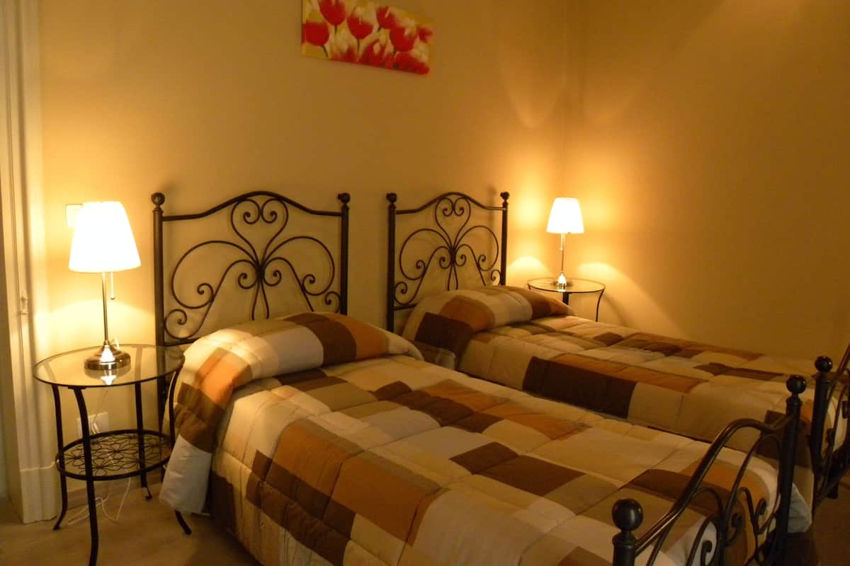 A double bed with a checkered bedspread, two bedside lamps, and a wall-mounted picture.