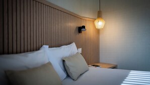Una habitación de hotel con cama, almohadas, mesita de noche y lámpara de pared.