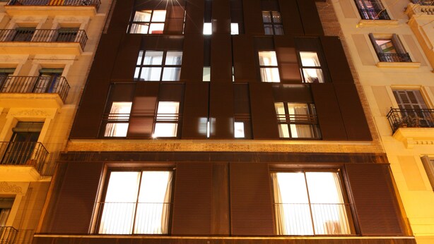 Un edificio de varios pisos con fachada moderna, amplios ventanales y un llamativo letrero que dice 'MH Apartments'.