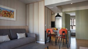 Una sala de estar moderna con sofá, mesa de comedor y sillas. Se observa una cocina al fondo, con una lámpara colgante.