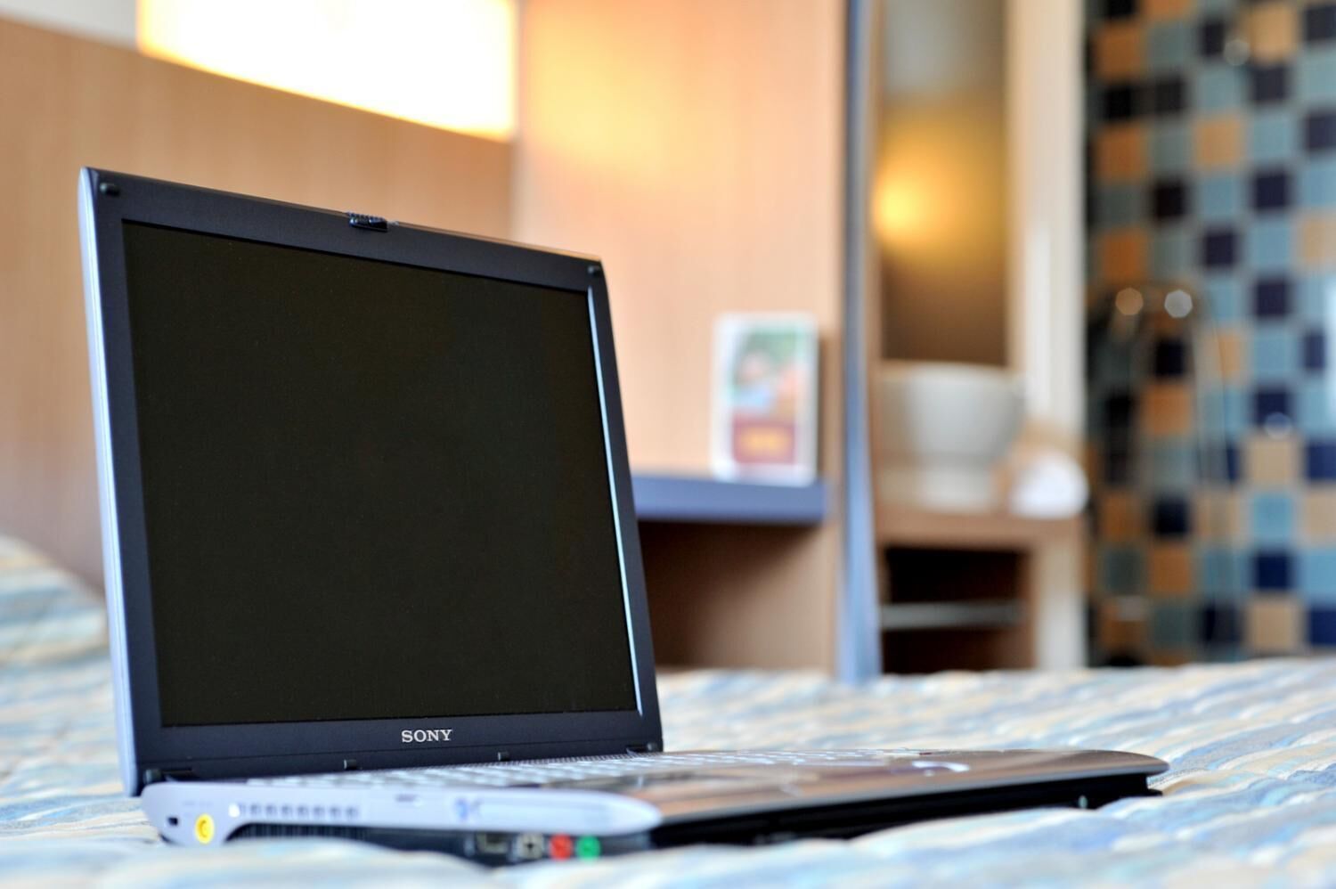 A Sony laptop on a bed with a checkered bedspread.