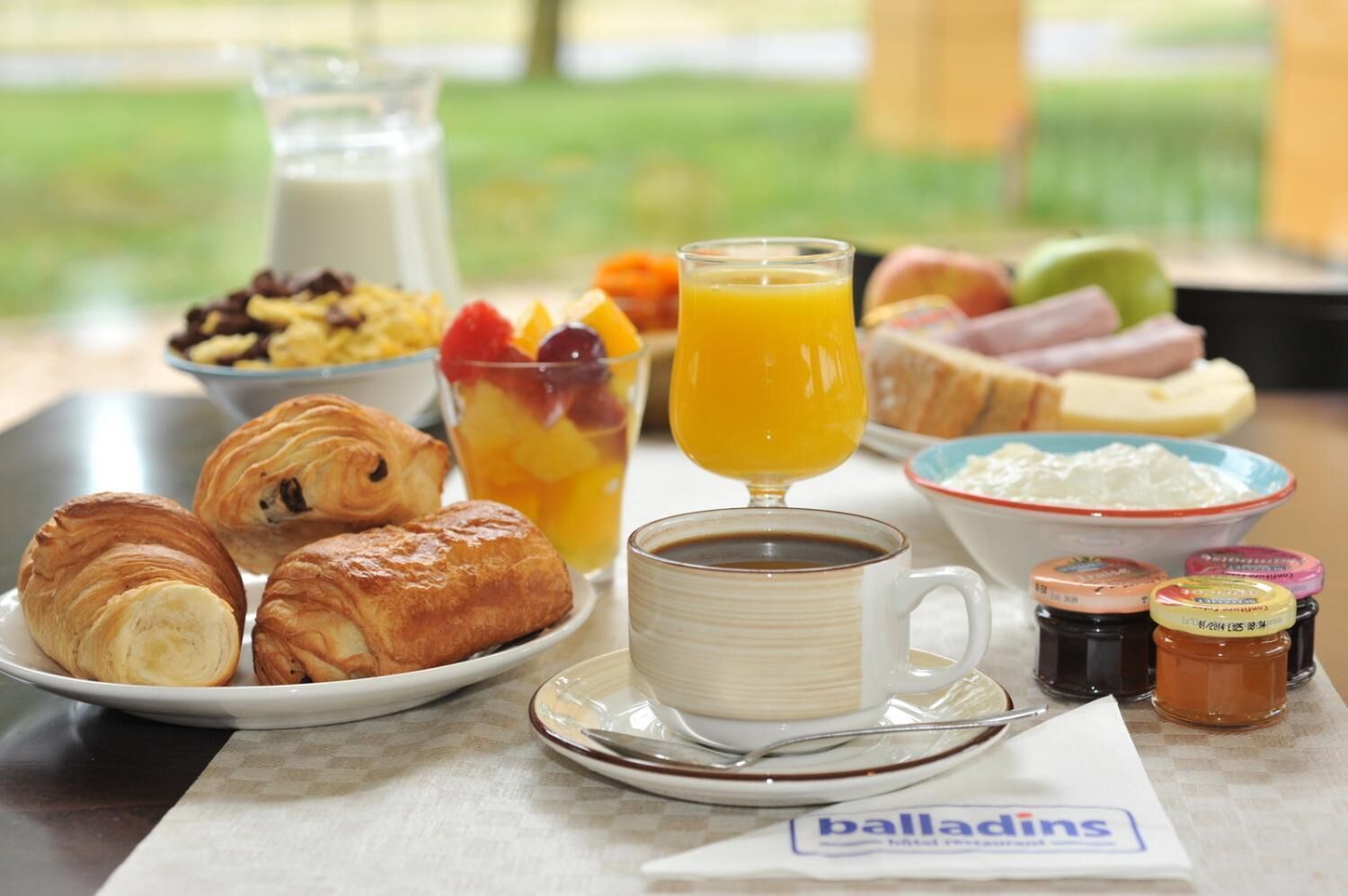 A breakfast setting with croissants, fruit, orange juice, coffee, and condiments on a table.