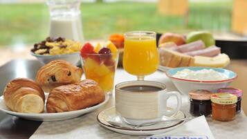 Une table dressée pour le petit-déjeuner, avec des croissants, des fruits, du jus d’orange, du café et divers condiments.
