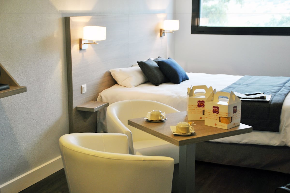 Ein Hotelzimmer mit einem Bett, einem Nachttisch mit Lampe, einem Sessel und einem Tisch mit Taschentüchern.