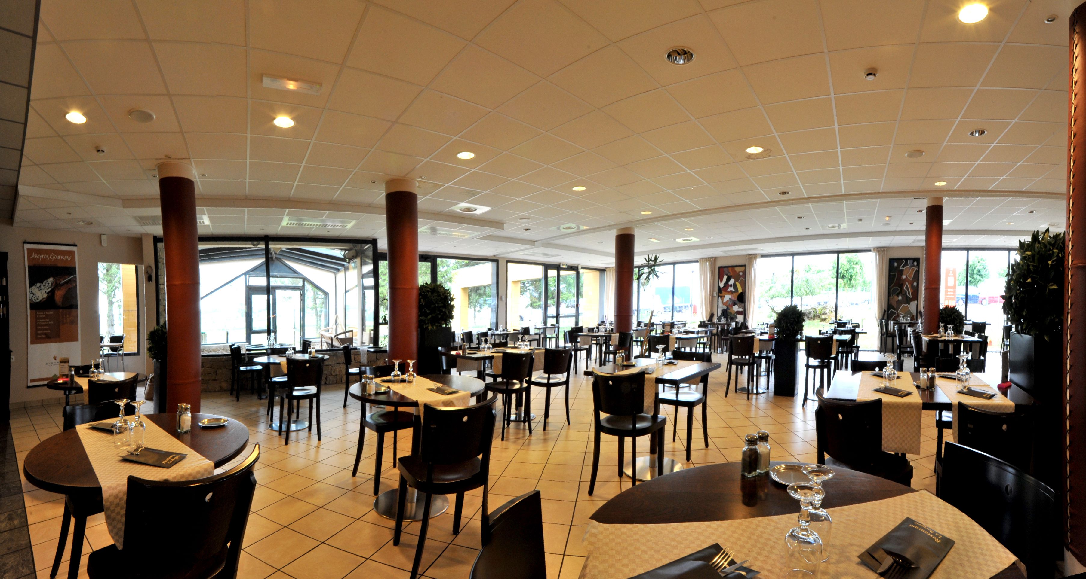 A spacious restaurant with multiple dining tables and chairs, large windows, and a high ceiling with recessed lighting.