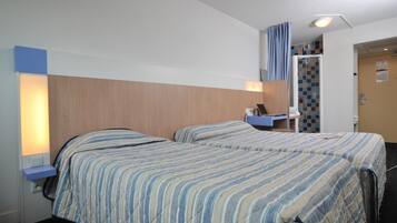 Habitación de hotel con dos camas, un escritorio con una computadora portátil, zona de ducha y un pequeño rincón de descanso.