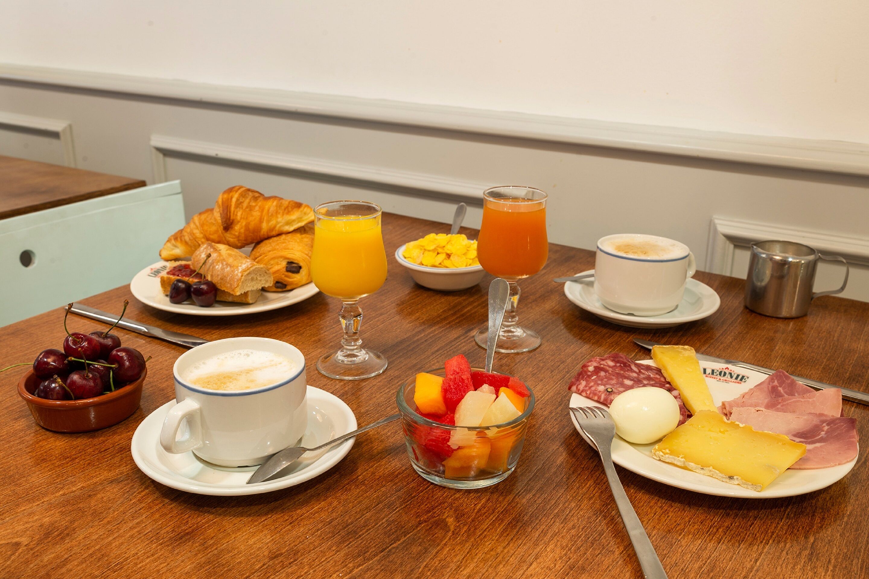 A breakfast table with croissants, fruit, cheese, ham, and beverages.