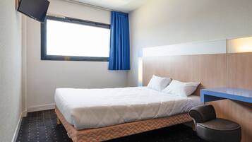A hotel room with a bed, a desk, a chair, a TV, and a window with curtains.