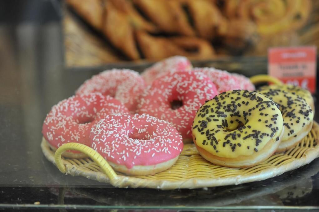 Una vitrina con varios pasteles, incluyendo donas rosadas y amarillas con chispas.