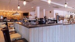 A bar area with a wooden counter, bar stools, hanging pendant lights, and a stone wall in the background.