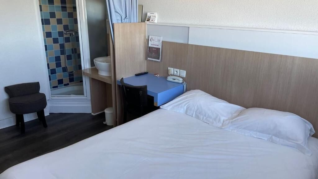 A hotel room with a bed, a desk, a chair, a shower, and a small seating area.