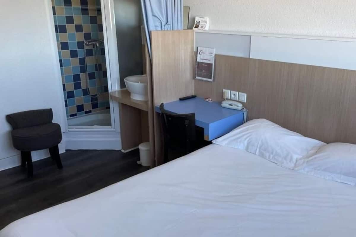 Ein Hotelzimmer mit Bett, Schreibtisch, Stuhl, Dusche und einer kleinen Sitzecke.