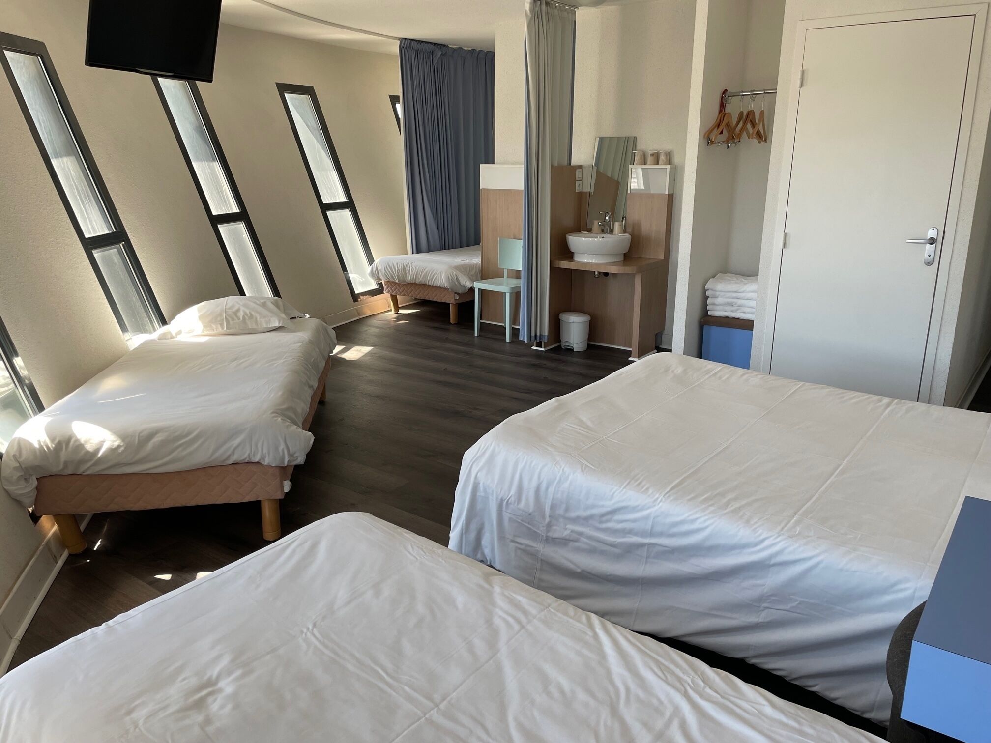 A hotel room with two beds, a bathroom with a sink and mirror, and large windows.