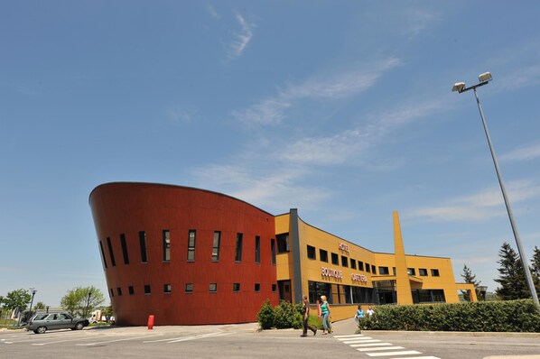A modern building with a curved red facade and a yellow section labeled "HOTEL BOUTIQUE CAFE."