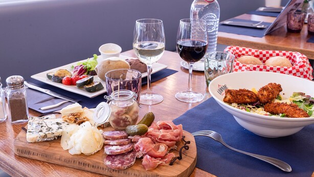 A dining table with a variety of food items, including cheese, cured meats, and a bowl of salad. There are also two glasses of wine and a bottle of water.