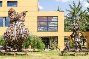 Un bâtiment moderne doté de grandes fenêtres et orné, au premier plan, d’une sculpture représentant une figure mécanique.