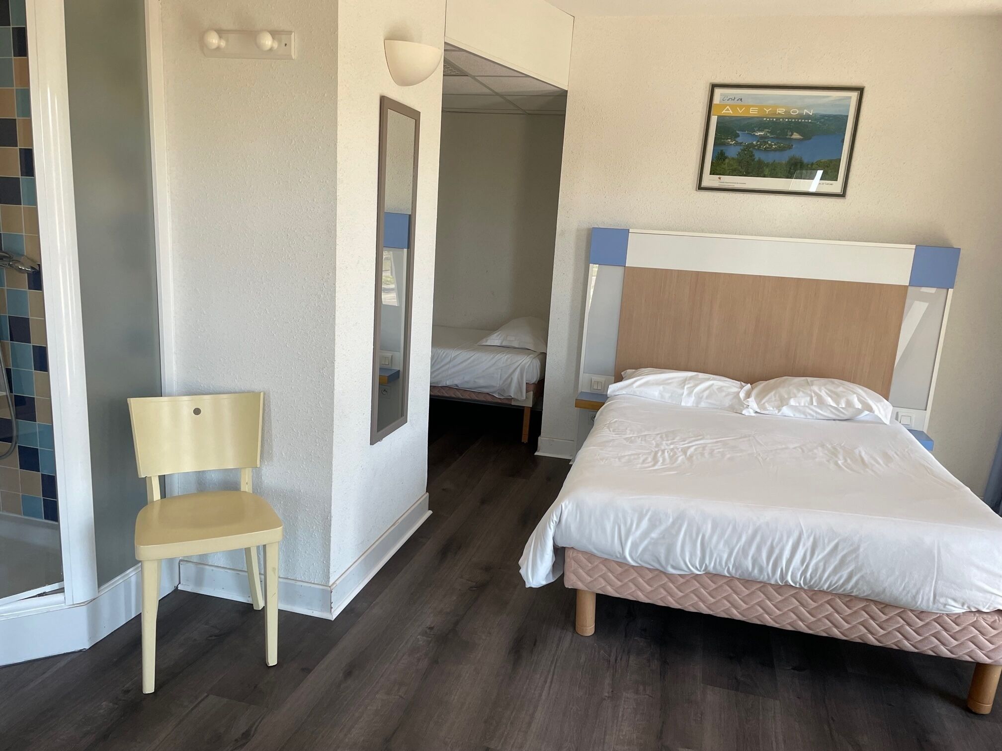 A bedroom with a bed, a chair, a mirror, and a framed picture on the wall.
