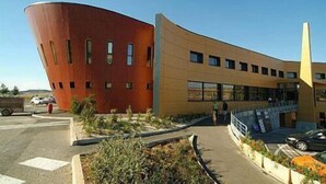 A modern building with a curved facade and a large, red structure adjacent to it.