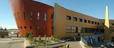 A modern building with a curved facade and a large, red structure adjacent to it.