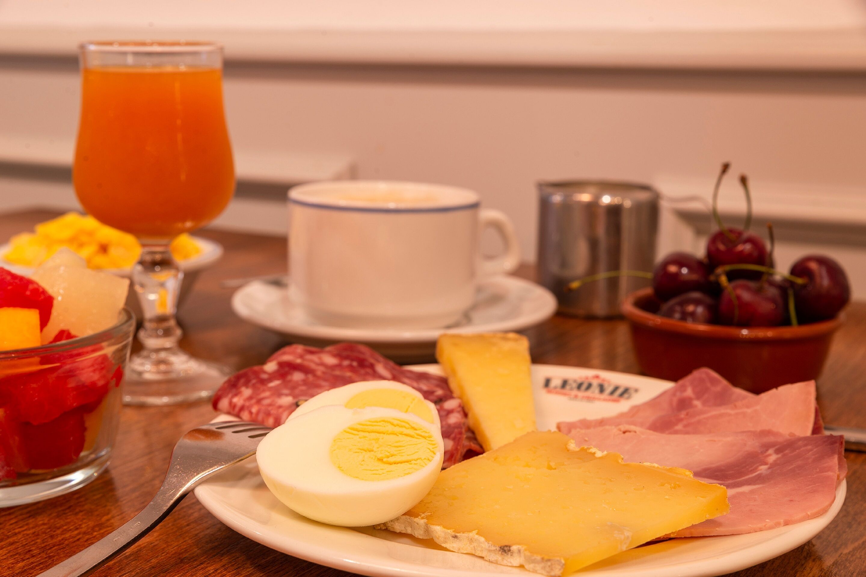 A breakfast setting with a plate of cheese, ham, and a boiled egg, a glass of orange juice, and a cup of coffee.
