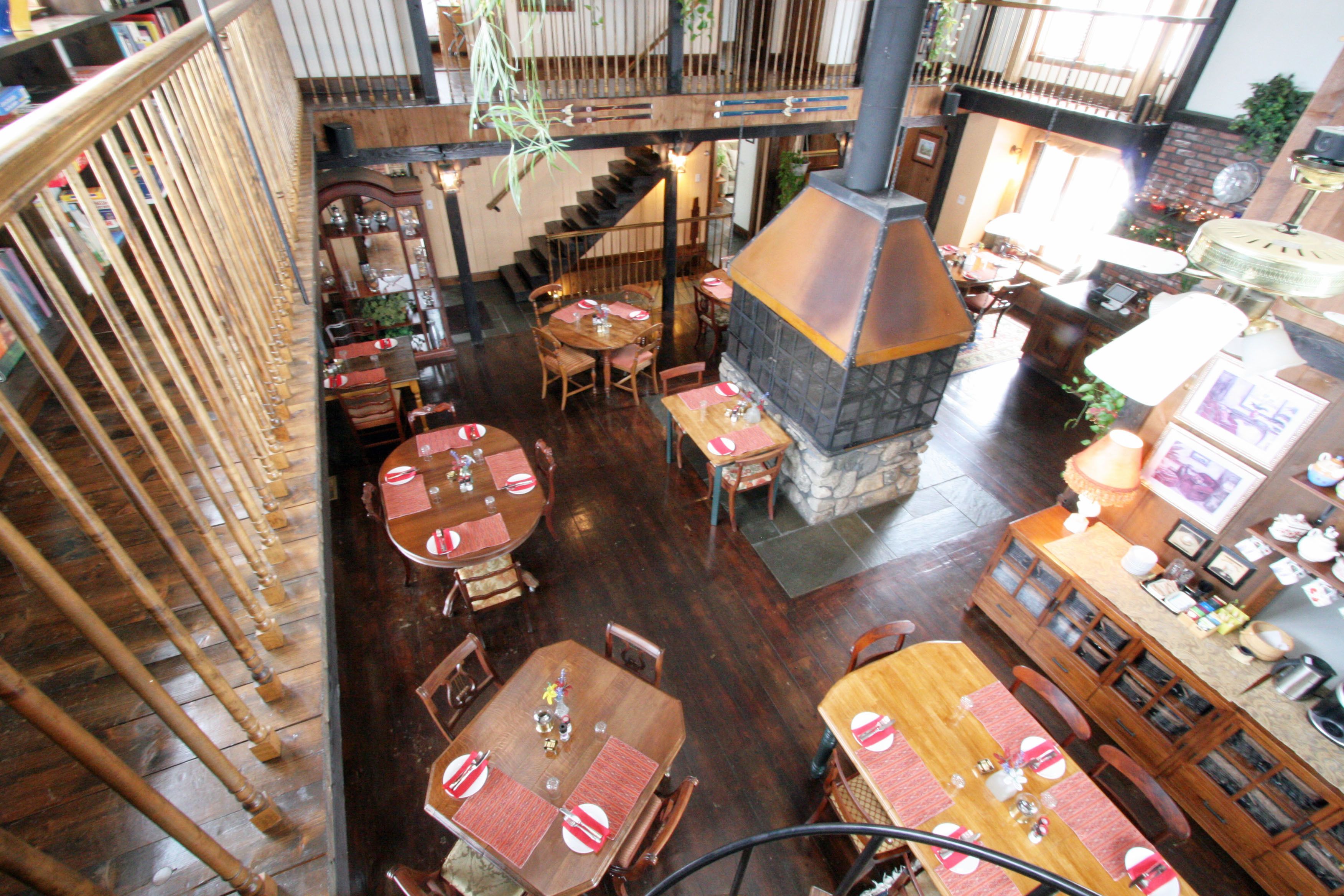 A spacious restaurant with multiple dining areas, a stone fireplace, and a wooden staircase connecting different levels.