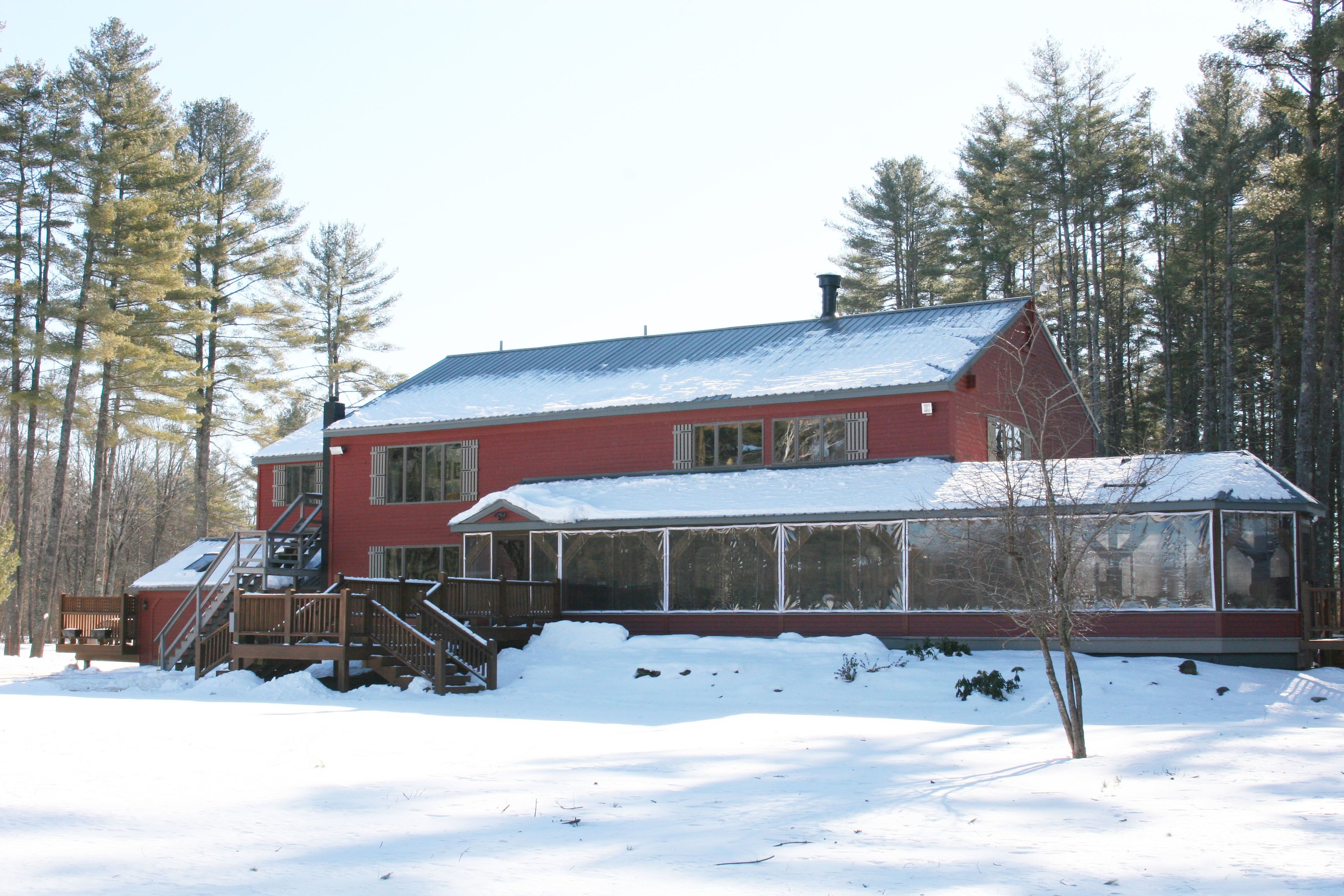 A red cabin with a large glass windowed porch, surrounded by snow and trees.