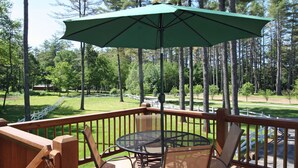 A wooden deck with a table and chairs, an umbrella, and a view of a park with trees and a white fence. - The Old Saco Inn (Fryeburg)