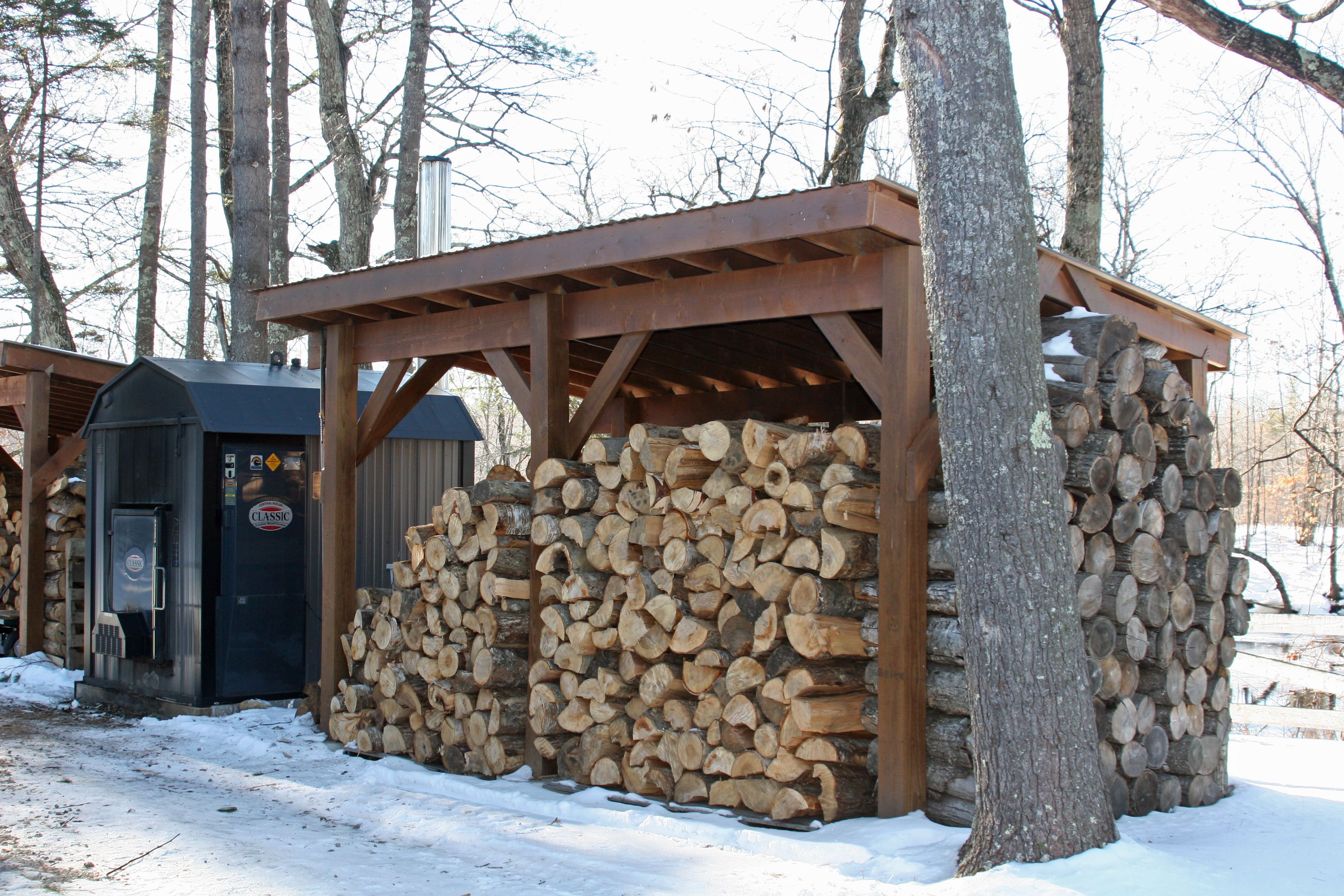 A rustic cabin with a wooden exterior, a black outhouse, and a stack of firewood.