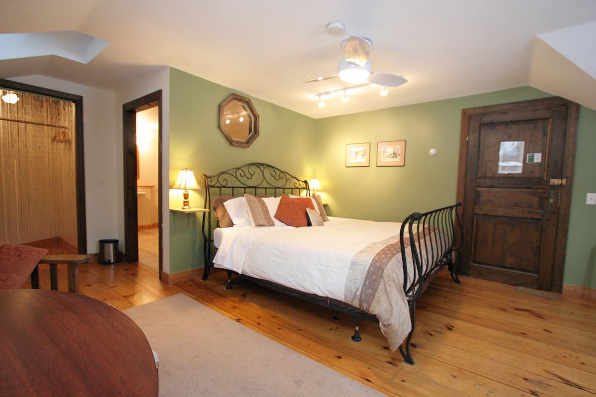 A bedroom with a bed, wooden floor, a ceiling fan, and a door.