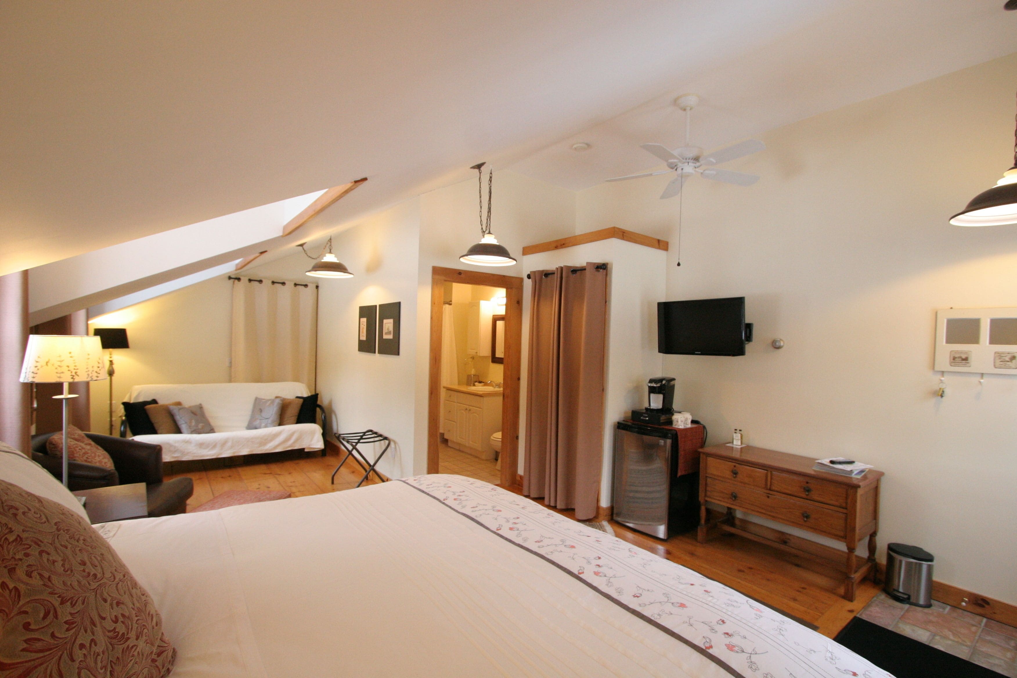 A bedroom with a bed, a desk, a chair, a television, and a ceiling fan.