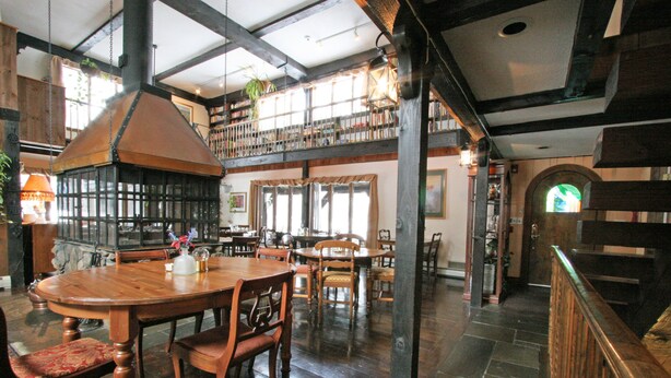 A spacious dining area with a large wooden table and chairs, a hanging light fixture, and a view of the upper level with bookshelves. - The Old Saco Inn (Fryeburg)