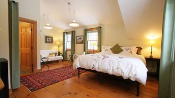 A bedroom with a wooden floor, a bed with a white bedspread, two windows with green curtains, a red rug, and a wooden door.