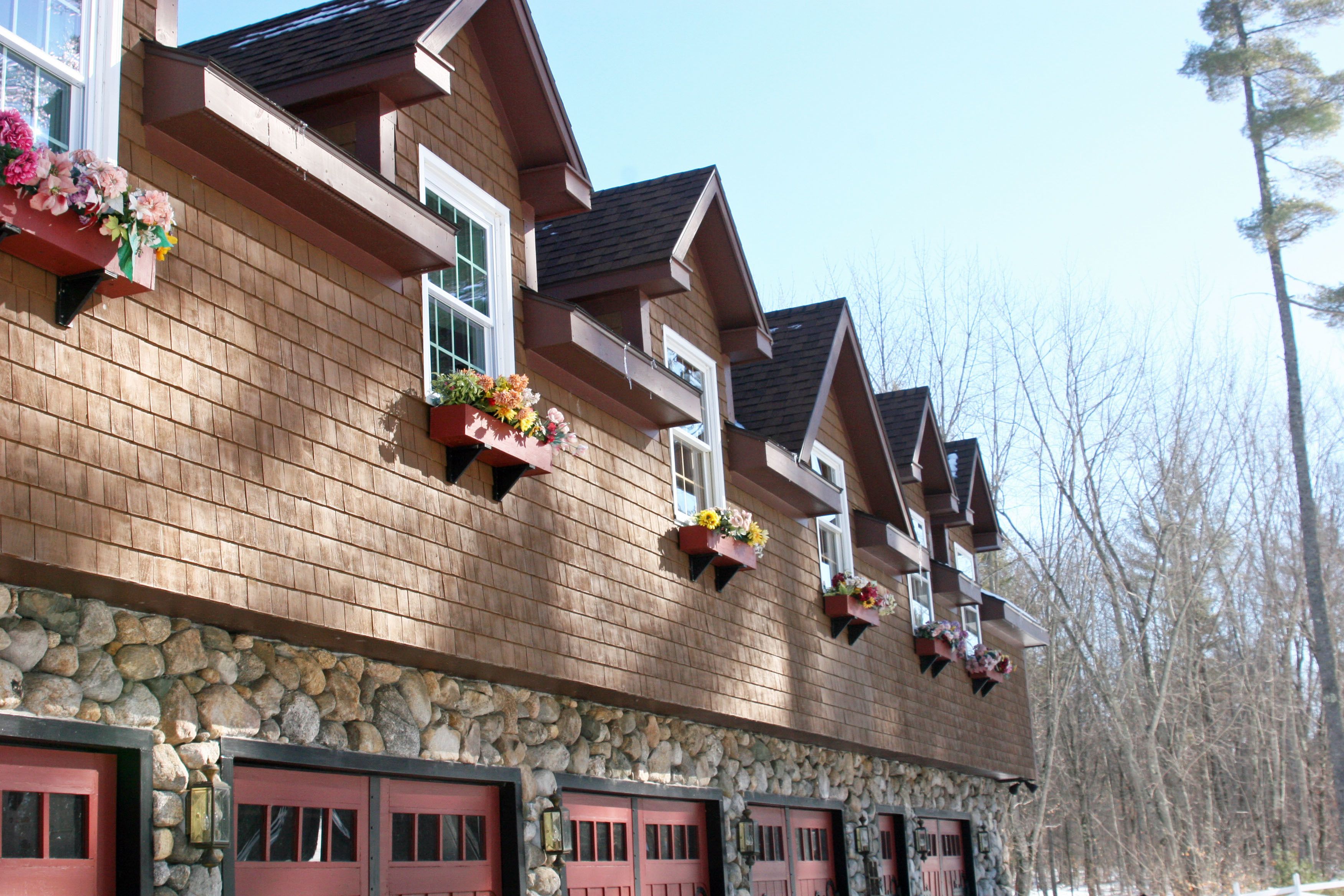 A wooden building with multiple windows and balconies, stone foundation, and red garage doors.